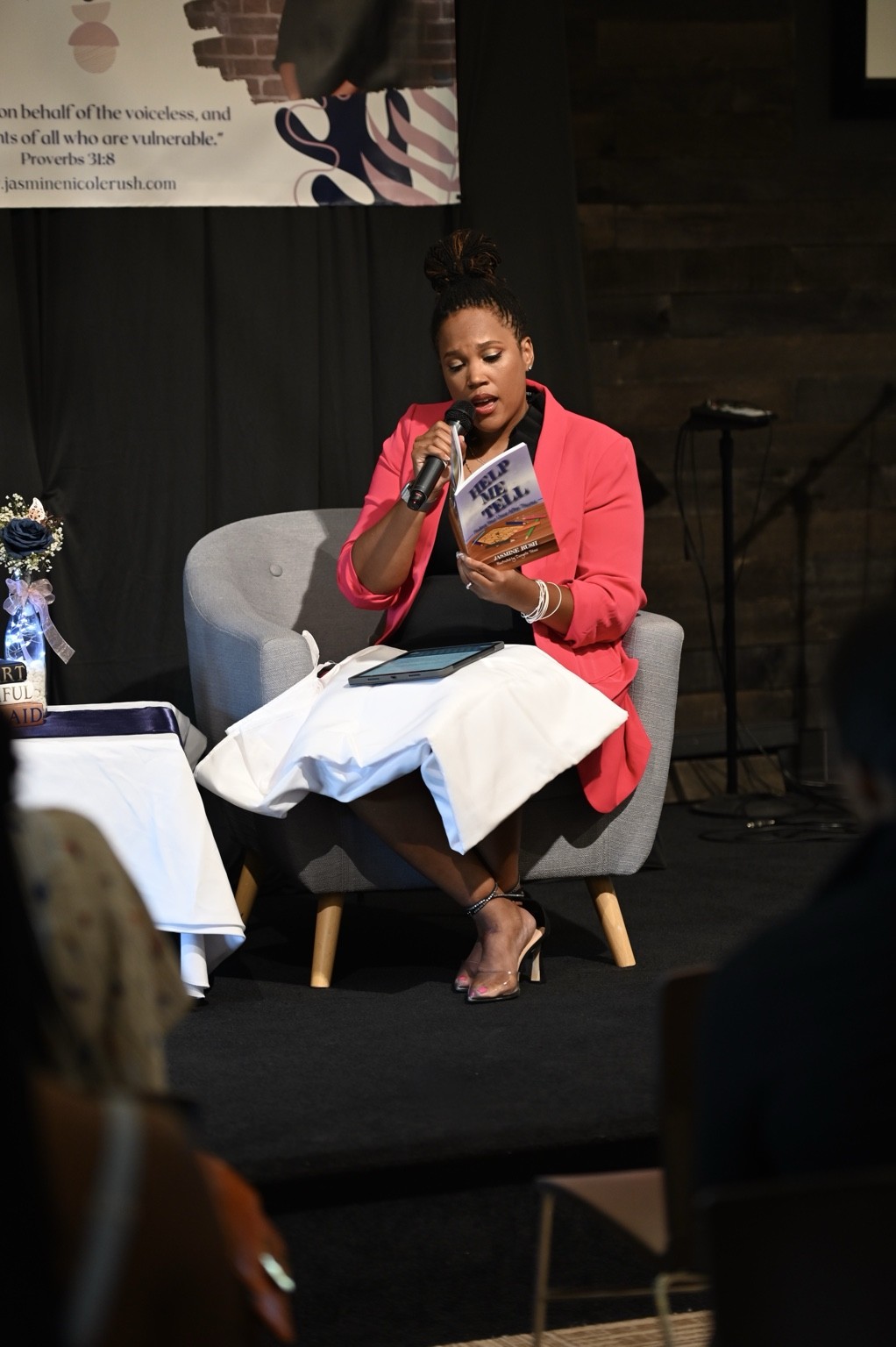 Jasmine Nicole Rush speaking into a microphone and reading from her book at a live event